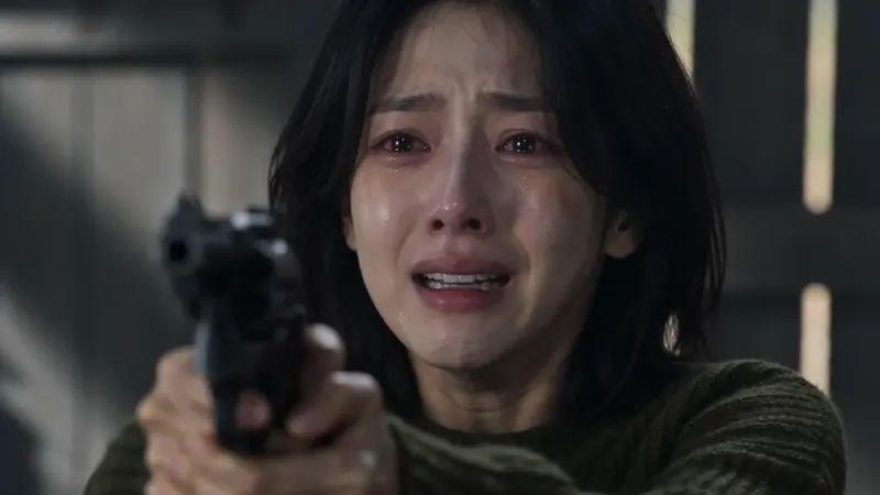A woman in tears aims a handgun in a dark wooden cabin